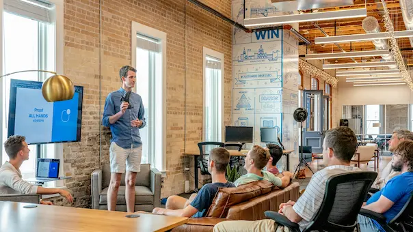 A person is delivering a presentation to a group of happy people inside an office.
